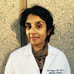 Headshot of a clinician in a white coat and scarf against a textured wall.